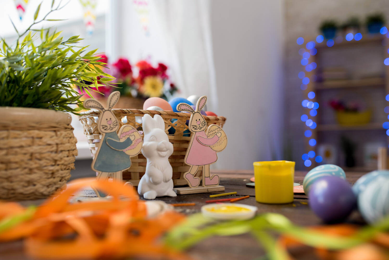 Background image of three Easter bunny figurines on decorated table with basket of eggs, copy space background